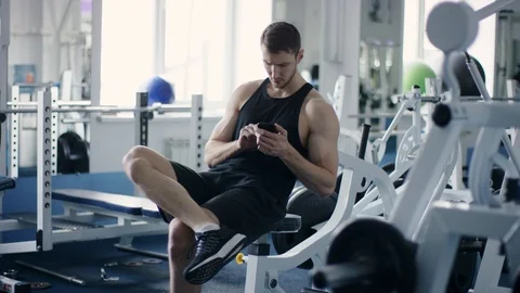 Young athlete texting on smartphone while resting during workout in a gym Stock Footage 105891893
