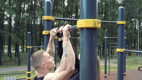 Young athletic couple doing pull-ups on the bar together outdoors Stock Footage 114360536