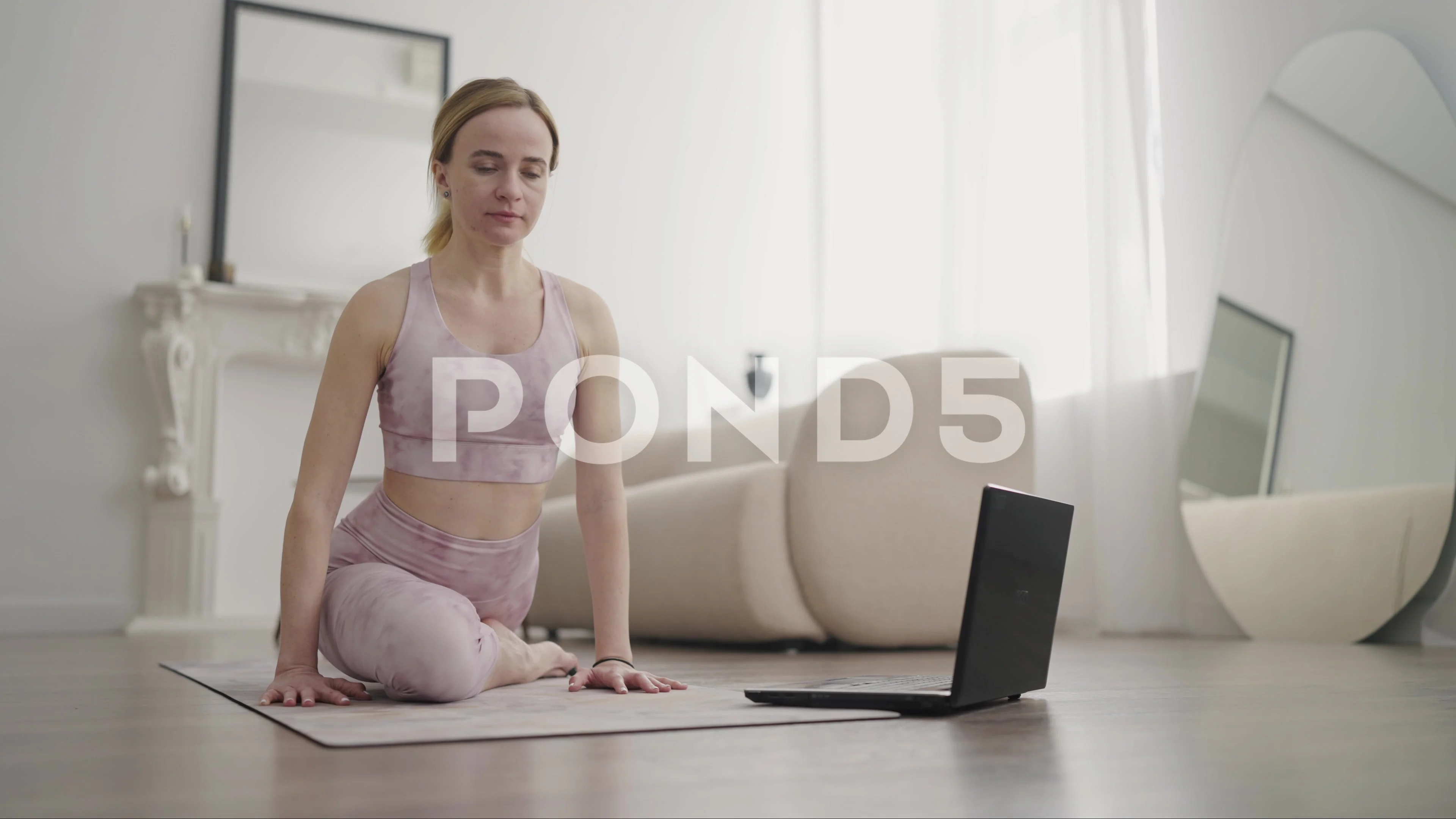 Woman doing yoga while watching instructional videos on laptop