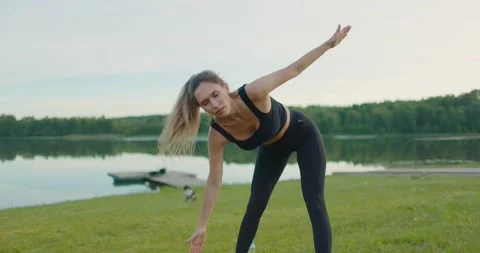 Young athletic girl performs exercise mill in fresh air on shore of lake Stock Footage 205575593