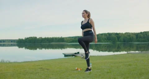 Young athletic girl performs exercise running on tspot in nature on lake shore Stock Footage 230991916