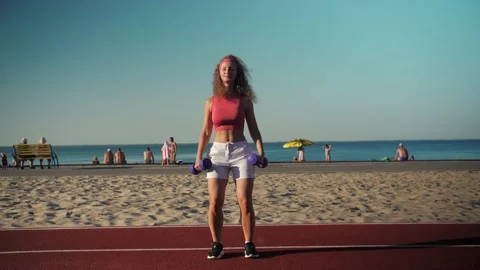 Young athletic girl training with weights on the beach.Dumbbell swings  Stock Footage 198884688