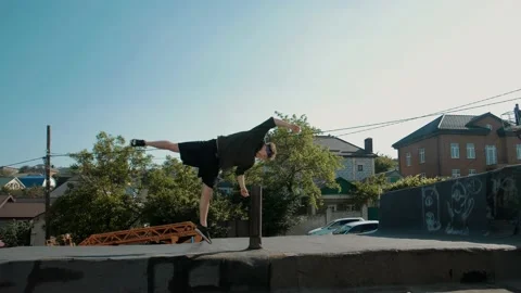 Young athletic guy runs and jumps somersaults on the roofs Stock Footage 130864632