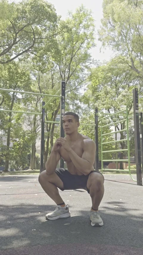 Young athletic man with a bare torso doing squat exercises in an outdoor gym. Video stock 326683646