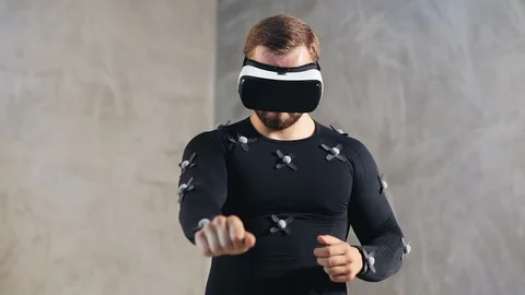 Young athletic man with beard wears motion capture suit with sensors and VR Stock Footage 93486045