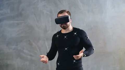 Young athletic man with beard wears motion capture suit with sensors and VR Stock Footage 93486647