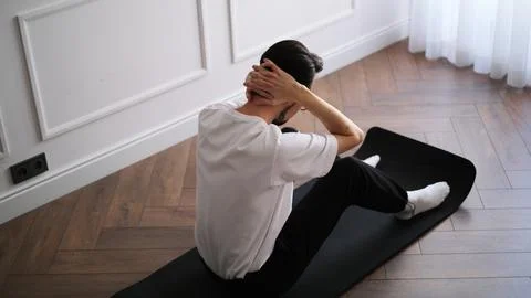 Young athletic man doing ab workout on a fitness mat at home in the early mornin Stock Photos