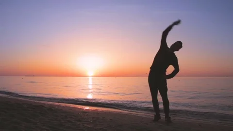 Young athletic man doing gymnastics on the sea early in the morning Vidéo 75324610