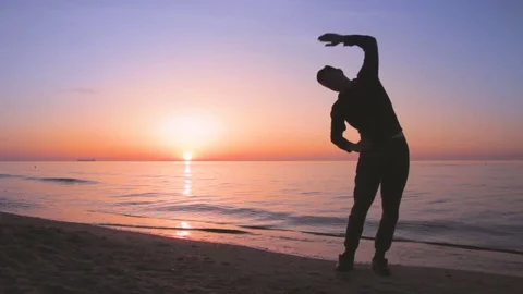 Young athletic man doing gymnastics on the sea early in the morning 库存影片 75785994