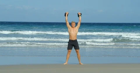 A young athletic man doing Kettlebell swings on a beach. Vídeo Stock 85510482