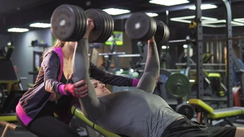 A young athletic man is engaged in a gym with dumbbells and a coach Stock Footage 78511465