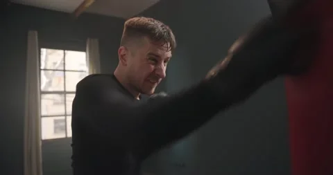 A young athletic man is hitting a boxing bag. Boxer practicing punches Stock Footage 145693239