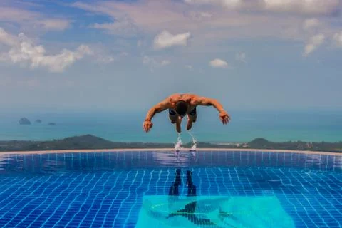 Young athletic man jumps into the pool at the top of the mountain Stock Photos