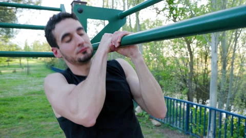 Young athletic man performing pull-ups on outdoor bars in a park setting Stock Footage 309795318