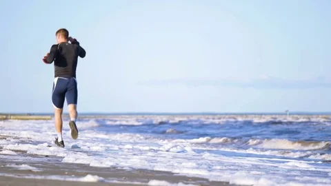 Young athletic man is running along the sea shore and dressing headphones Stock Footage 82410585