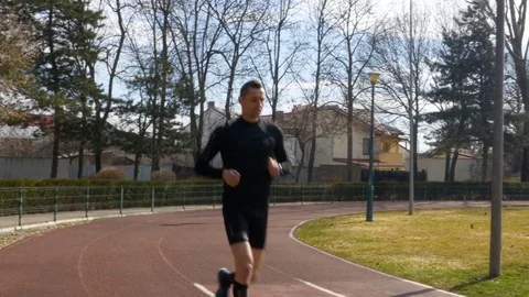 Young athletic man running in the park on the course track Stock Footage 74597685