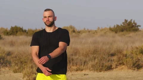 Young athletic man with smartwatch stretching arms before outdoors workout Video stock 132166477