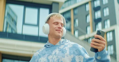 A young athletic man smiles as he puts on wireless headphones and selects a song 動画素材 303597434
