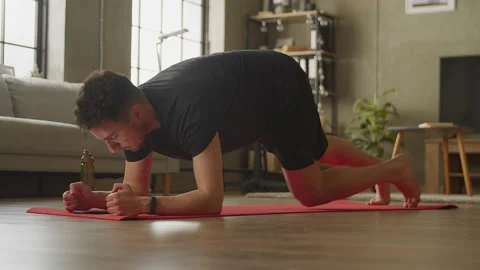 Young athletic man is standing in elbow plank, workouting in the morning at home Stock Footage 169015052
