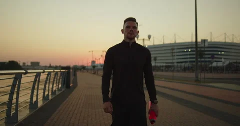 Young athletic man walking alone after workout on a city pier at sunset Stock Footage 276542638