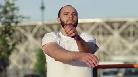 Young athletic man in white t-shirt rotating his hands to warm up outdoors Stock Footage 143496530