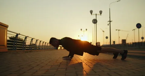 Young athletic man working out doing push-ups on a city street at sunset Stock Footage 276545949