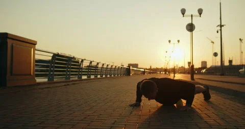 Young athletic man works out doing push-ups on a city street at sunset Stock Footage 276545321