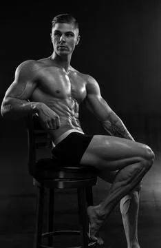 Young athletic shirtless man posing in shorts while sitting on chair in studio Stock Photos