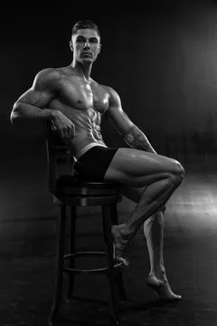 Young athletic shirtless man posing in shorts while sitting on chair in studio Stock Photos