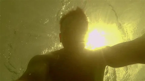 Young athletic young man under water waving at camera in backlight sunlight Stock Footage 71024510