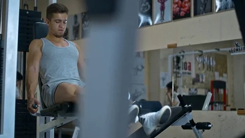 Young athlitic man does leg extensions in gym Stock Footage 81418759