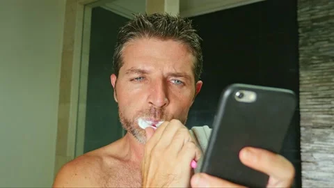 Young attractive and happy man brush teeth and watching phone at bathroom Stock Footage