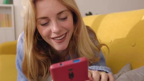 Young attractive blonde woman using mobile phone device while lying down on sofa Stock Footage 269082953