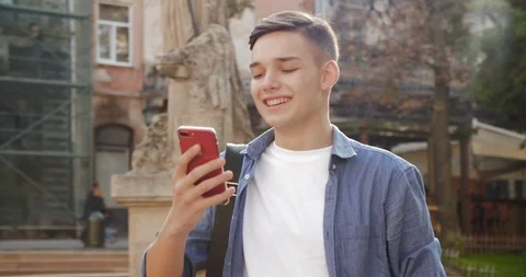 Young Attractive Boy smiles charmingly while Texting Message on his Smartphone Stock Footage 112156804