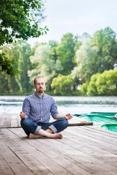 Young attractive breaded man with closed eyes  sitting on wooden pier, relaxing Stock Photos
