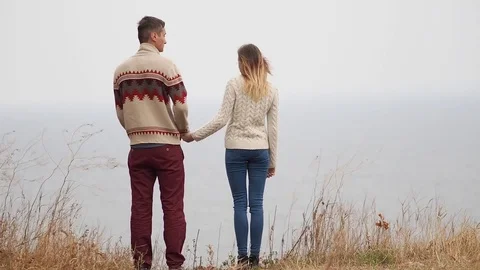 Young attractive couple in knitted sweaters on a cliff on sea shore Stock-Footage 70358977