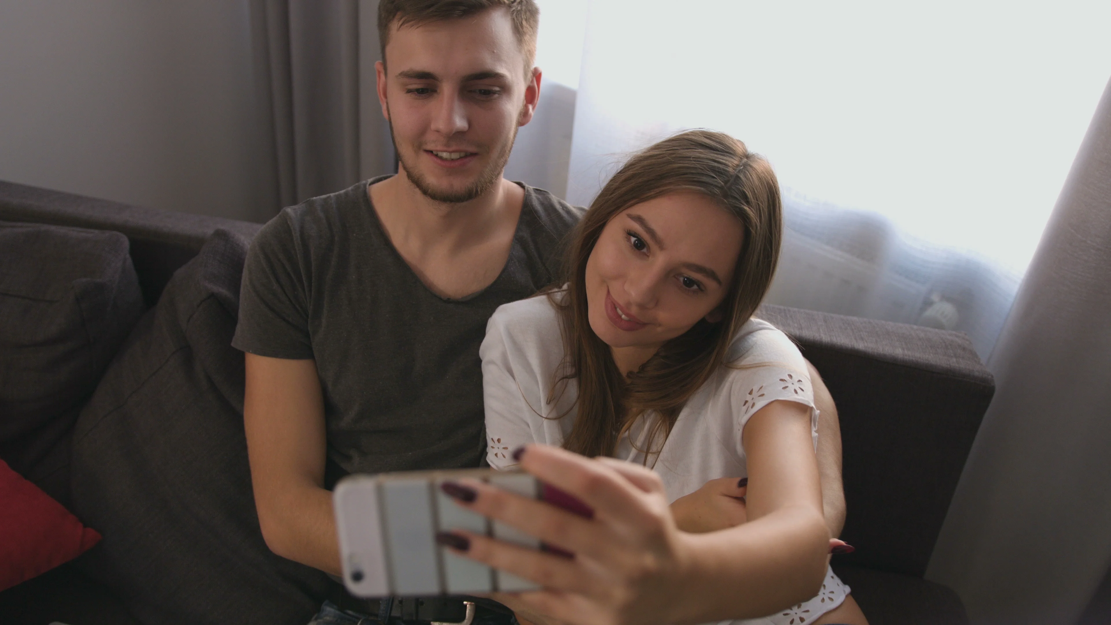 Young attractive couple in love making a selfie while sitting on sofa at  home