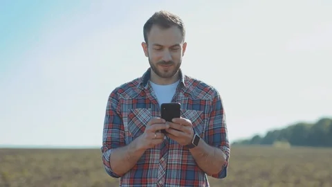 Young attractive farmer using a smartphone in the farmland in sunny weather 스톡 동영상 110942747