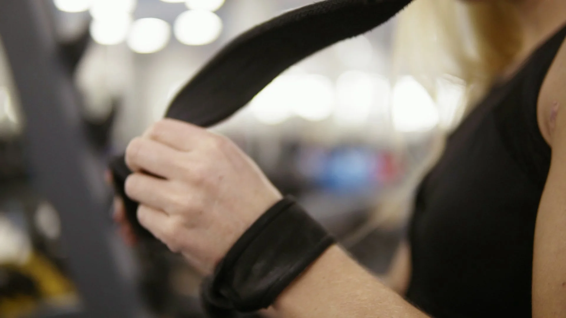 Young attractive female bodybuilder ties fitness straps around  barbellpreparing