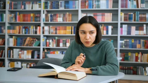 Young attractive female student reads a book and takes notes in a notebook Stock Footage