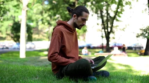 Young attractive freelance man using modern laptop sitting in sunny green park e 스톡 동영상 139145335