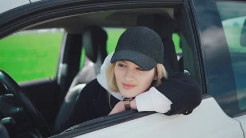 Young attractive girl in a black cap sits in an electric car and smiles at the 库存影片 156133653