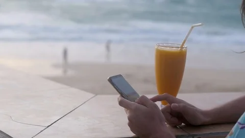 Young attractive girl using mobile phone drinking healthy juice on the beach 스톡 동영상 127614977