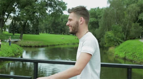 A young attractive guy with a beard is walking over a small bridge across river. Stock Footage 67271197