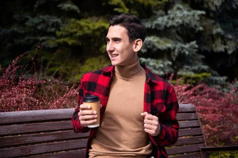 Young attractive guy drinks coffee in the autumn park. Stock Photos
