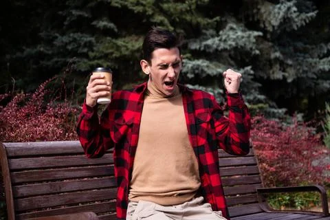 Young attractive guy drinks coffee in the autumn park. Stock Photos