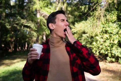 Young attractive guy drinks coffee in the autumn park. Stock Photos