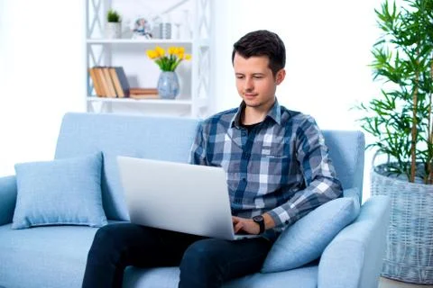 A Young attractive guy man is browsing at his laptop, sitting at home on the  Stock Photos