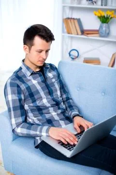 A Young attractive guy man is browsing at his laptop, sitting at home on the  Stock Photos