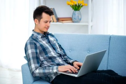 A Young attractive guy man is browsing at his laptop, sitting at home on the  Stock Photos